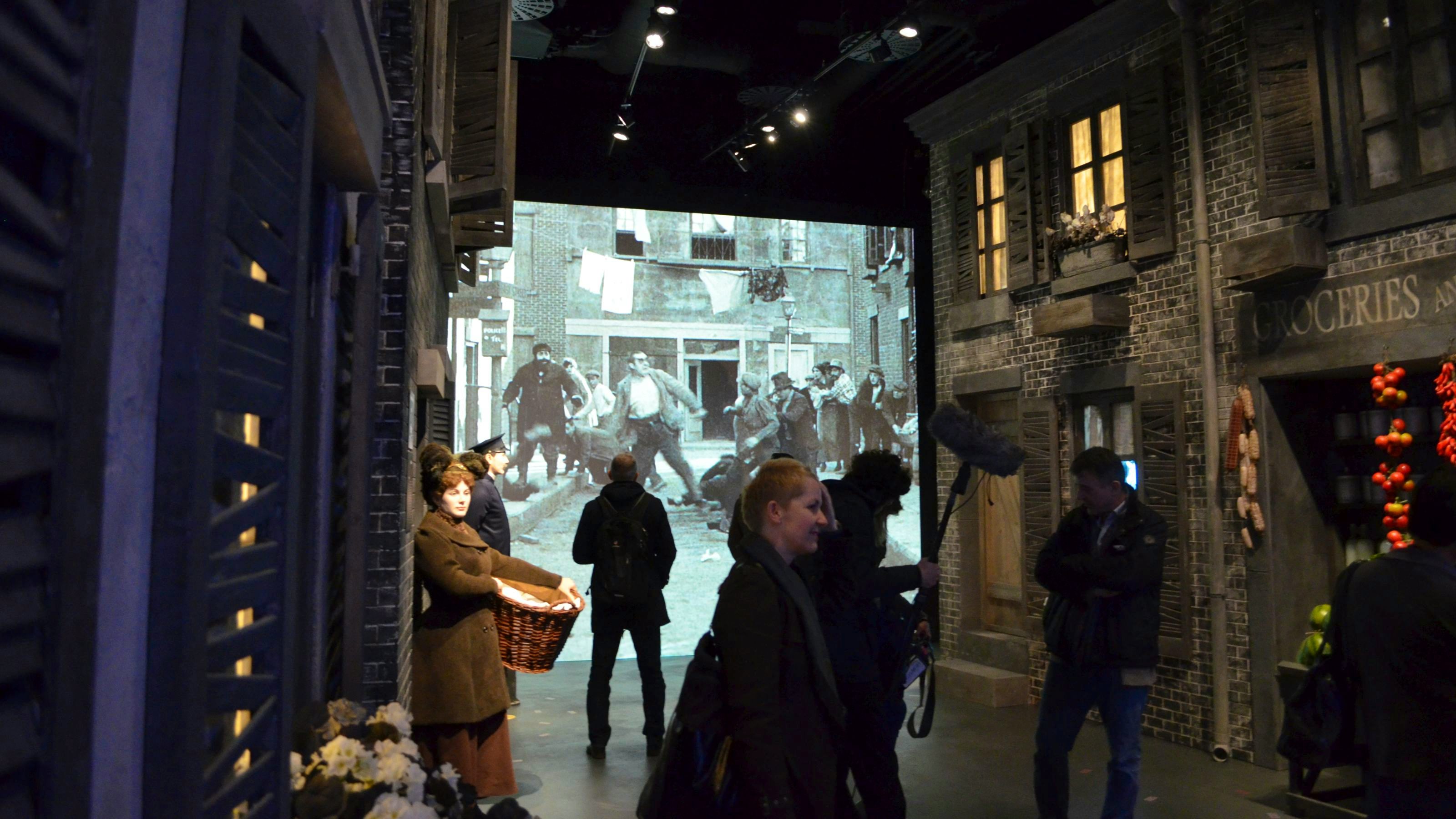 Visitors walk through recreated film sets as a silent film is shown on a screen in the background.