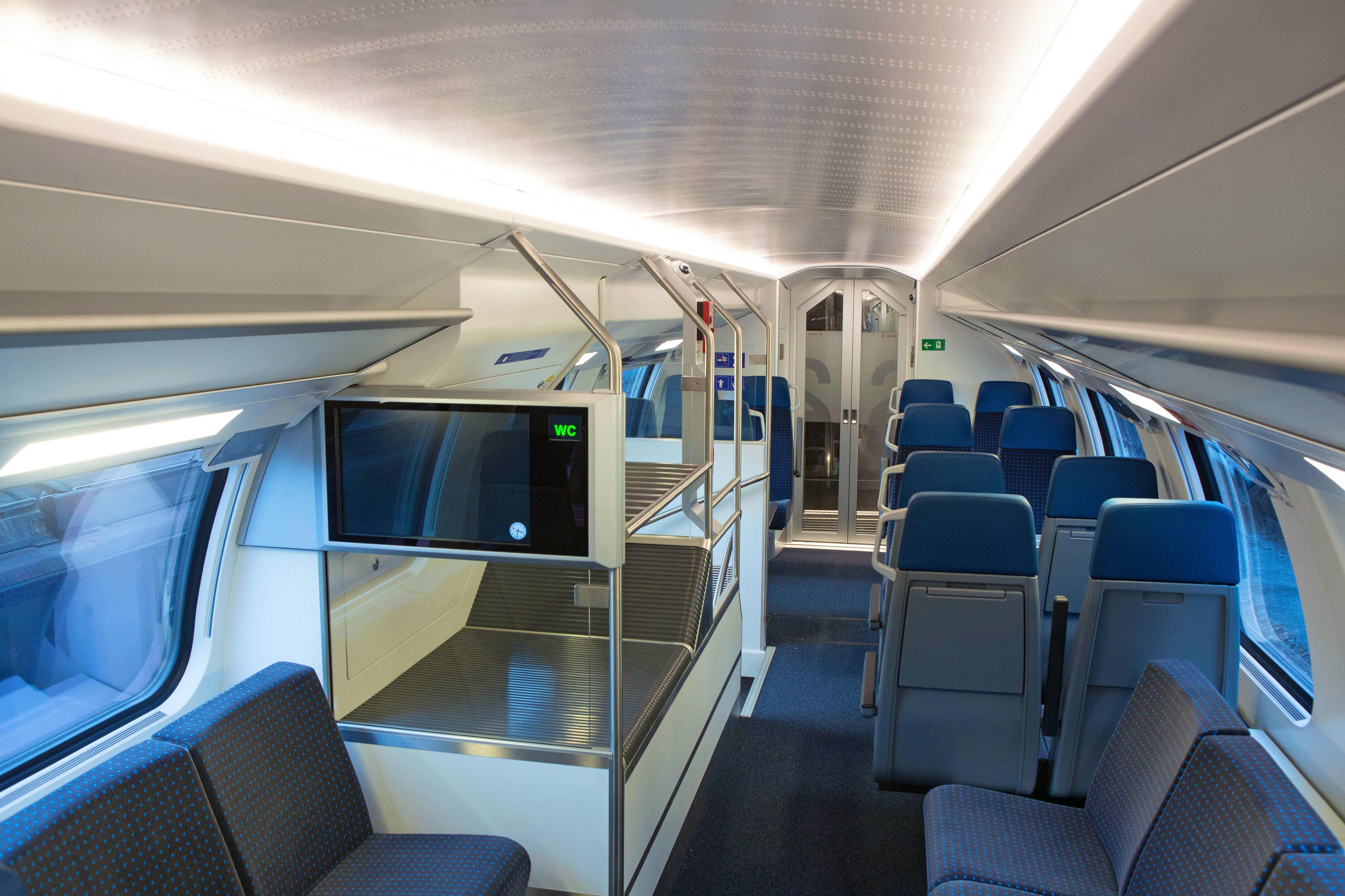 Allestimento interno di 2ª classe – I sedili sono di colore blu scuro. A sinistra del corridoio si trovano un monitor informativo e un supporto portabagagli, dietro il quale è posta una scala che conduce al piano inferiore. Sono disponibili sia sedili nel