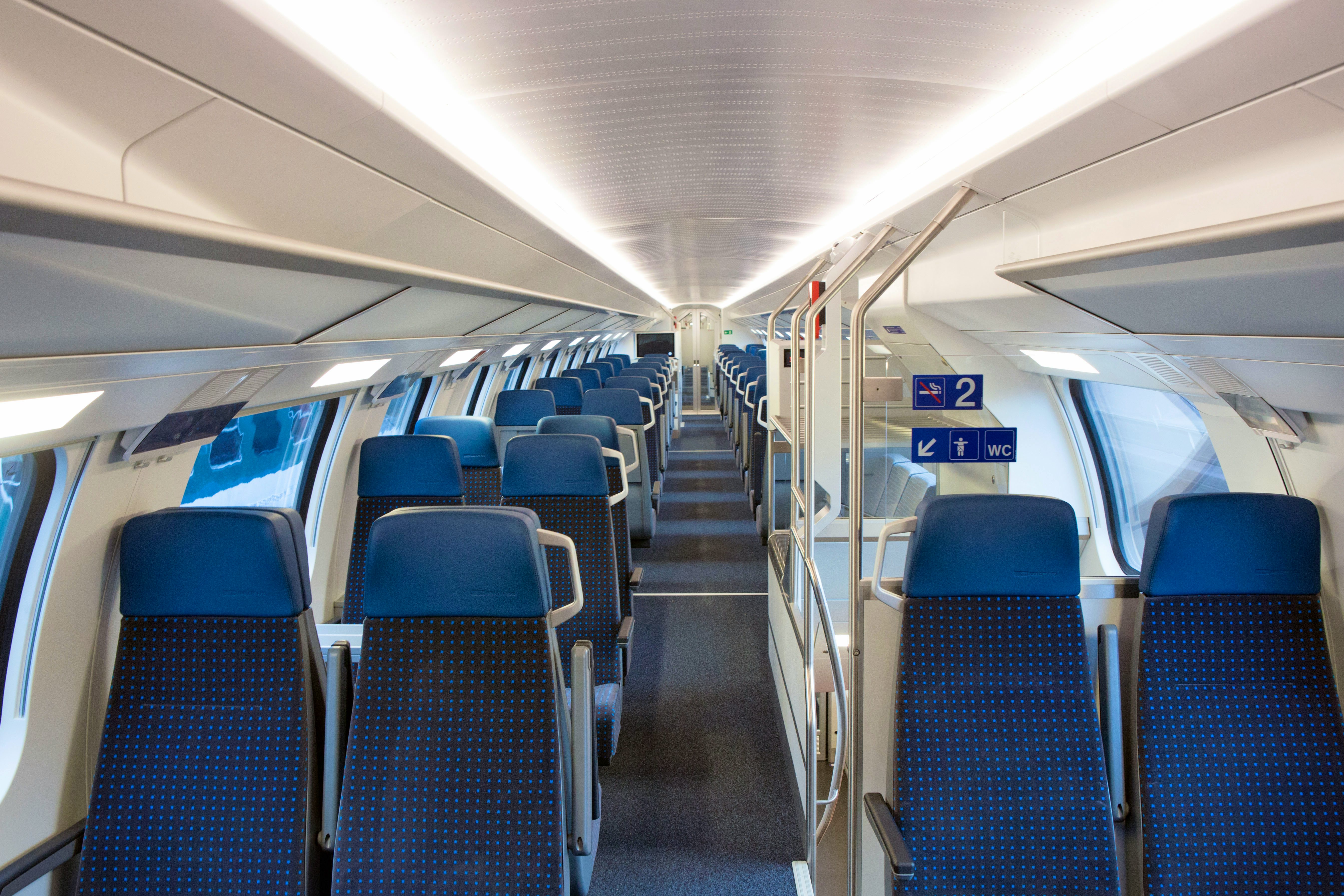 Allestimento interno di 2ª classe – Da entrambi i lati del corridoio si trovano compartimenti da quattro posti. I sedili sono di colore blu scuro. Sulla destra, tra i compartimenti si scorge una scala che conduce al piano inferiore. 