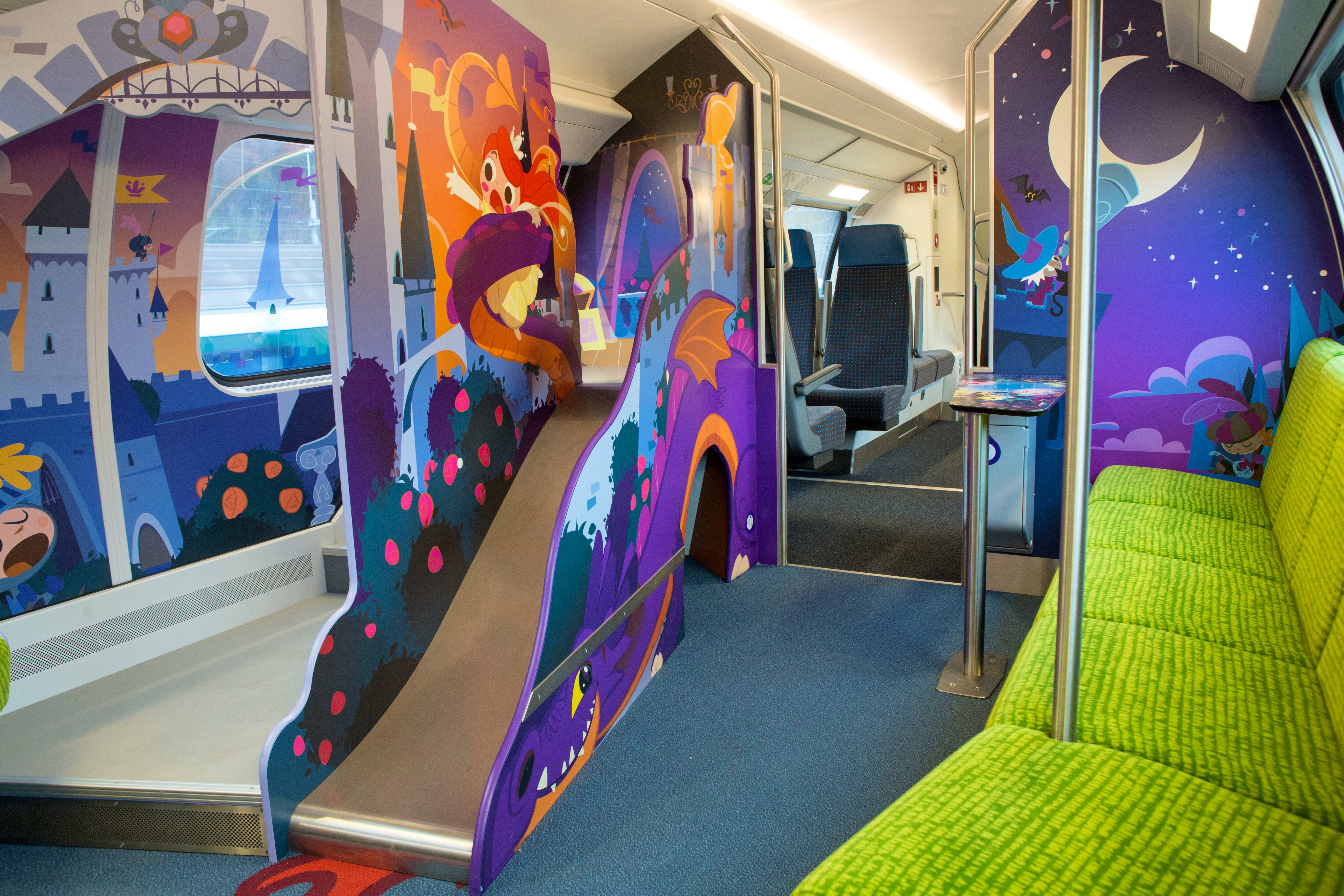 Carrozza famiglia sull’IC 200 – Al centro della carrozza si trova un piccolo scivolo su cui è raffigurato un drago. Sulla destra si trova una fila di sedili color verde chiaro.