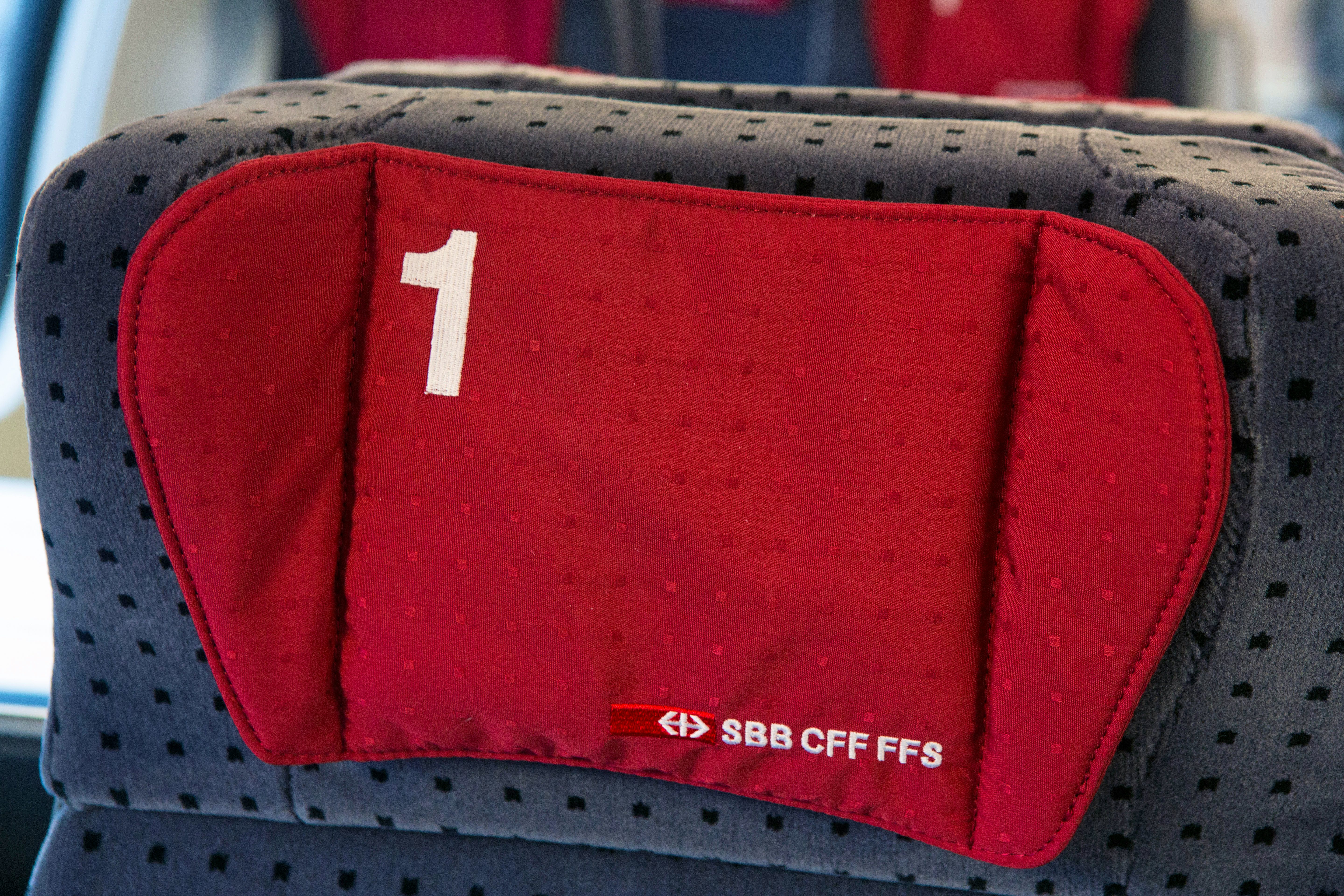 Allestimento interno di 1ª classe – A sinistra del corridoio centrale si trovano i compartimenti da quattro posti e a sinistra quelli da due. I sedili sono di colore grigio scuro con piccoli cuscini rossi sui poggiatesta.